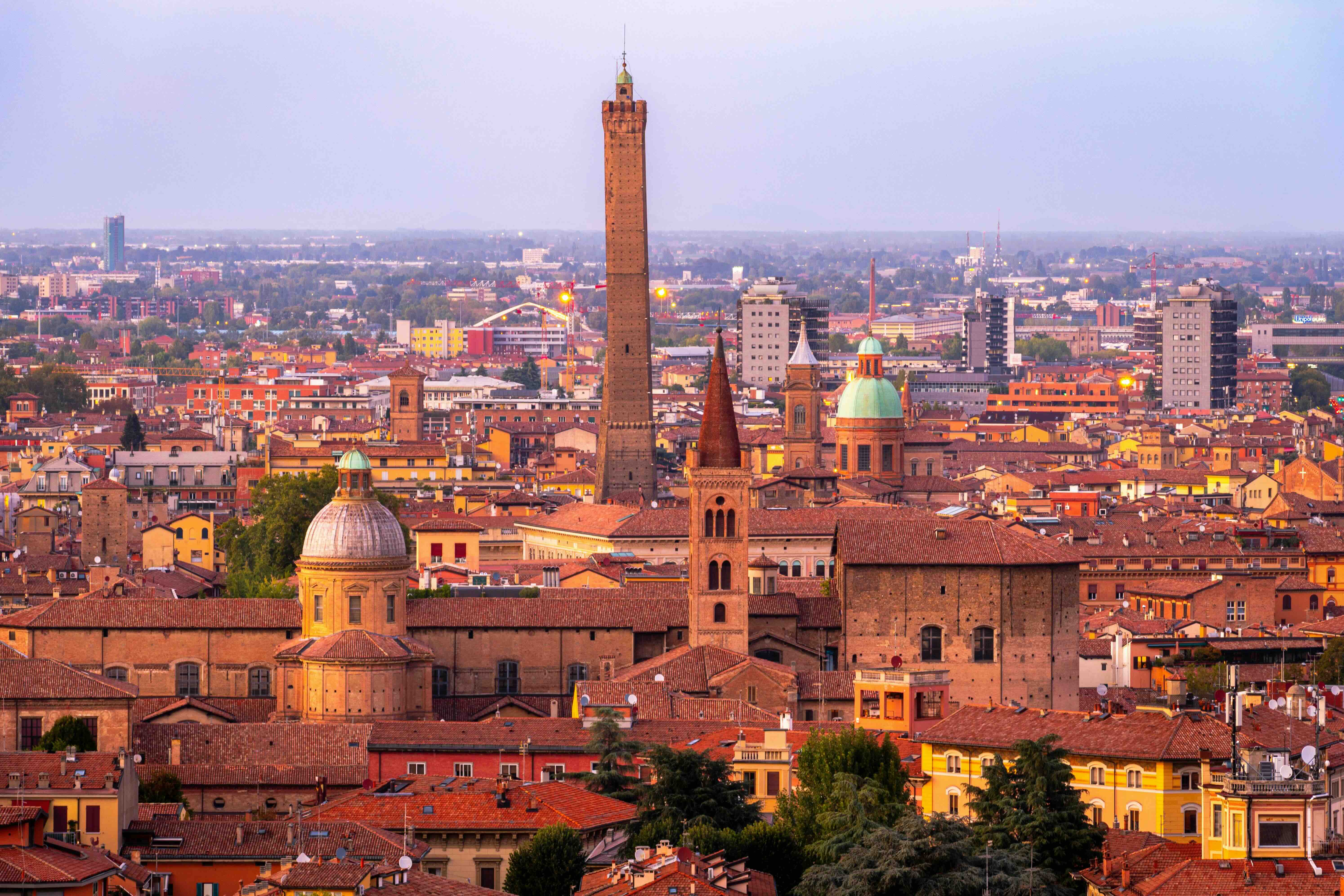 The terracotta rooftops and medieval towers of Bologna's old city at dusk, with the Asinelli tower rising above