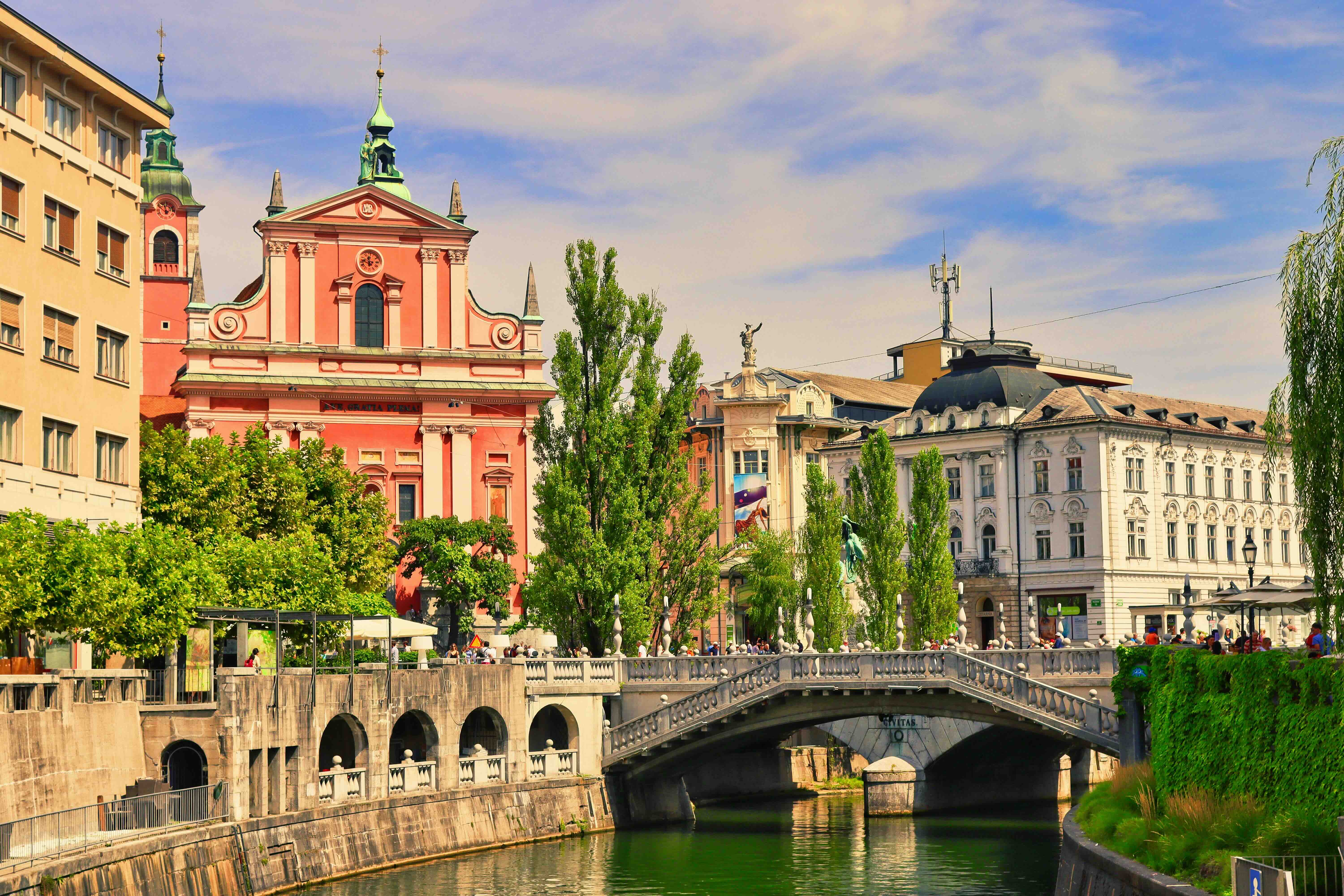 The pink Baroque Franciscan Church of the Annunciation on Prešeren Square in central Ljubljana, beside a stone bridge over the willow-lined Ljubljanica river