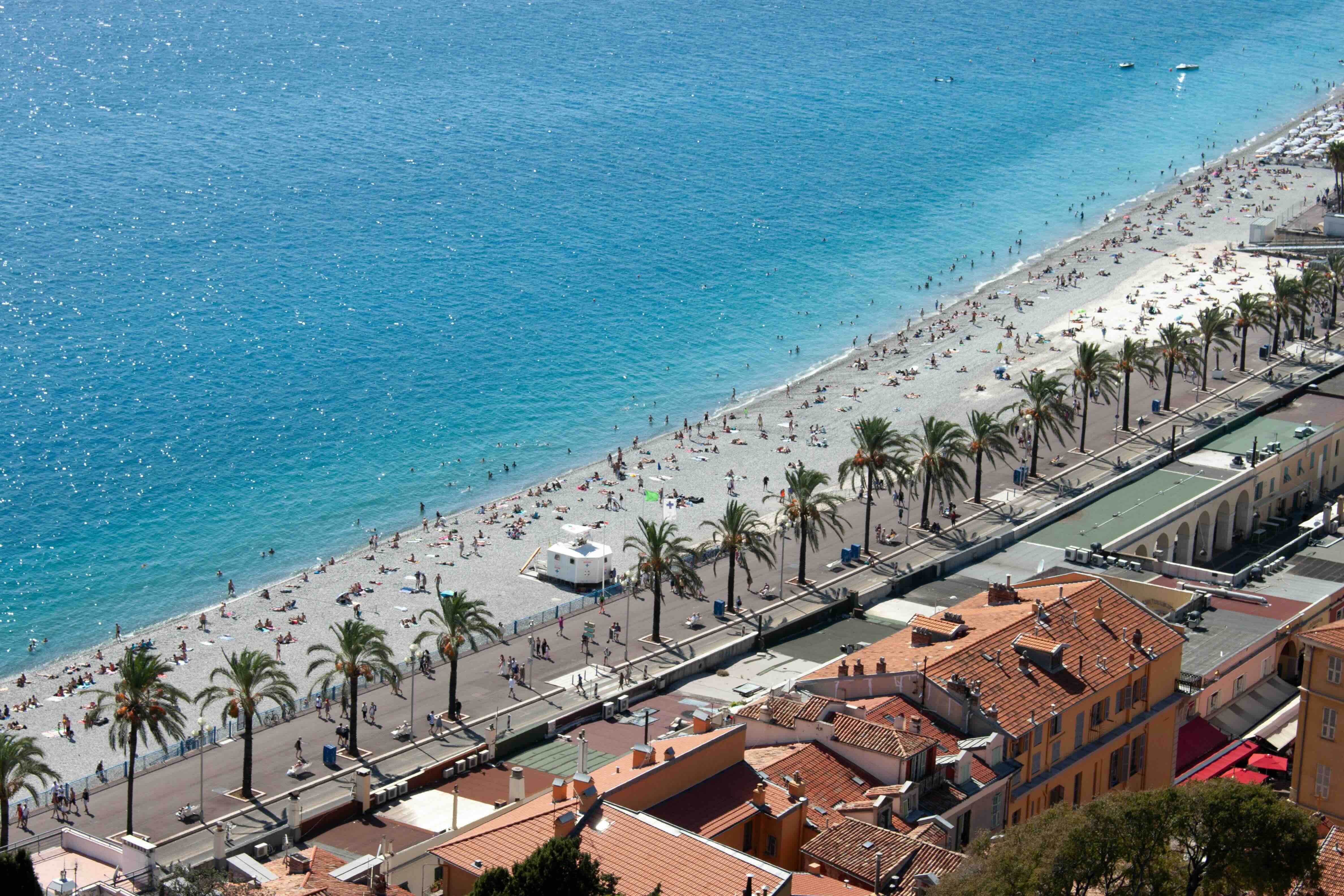The palm-lined Promenade des Anglais curving along Nice's pebble beach and the turquoise Baie des Anges, with the terracotta rooftops of the old town below
