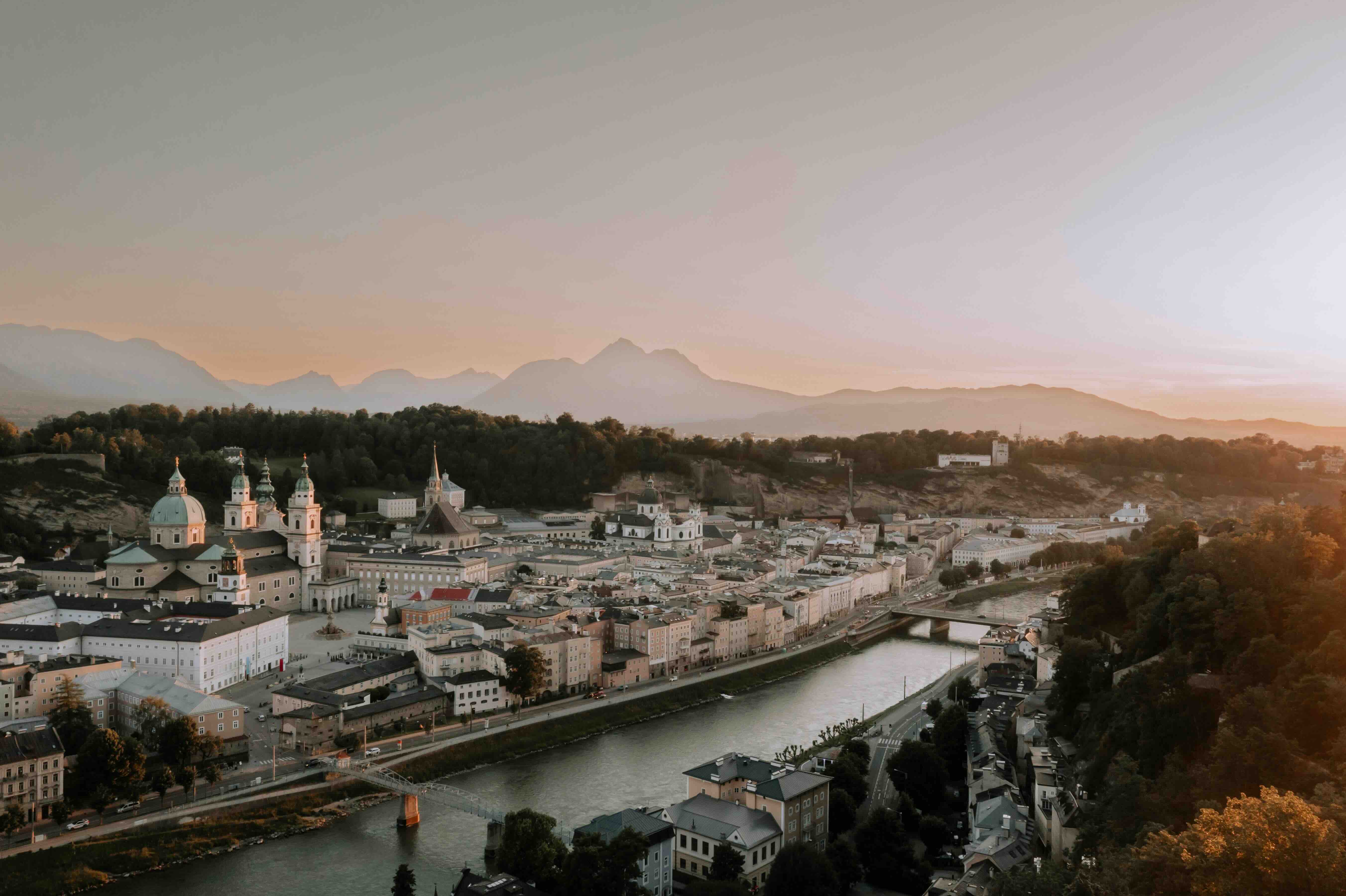 Salzburg's baroque old town, its cathedral domes and church spires beside the Salzach river, with the Alpine foothills glowing at sunset