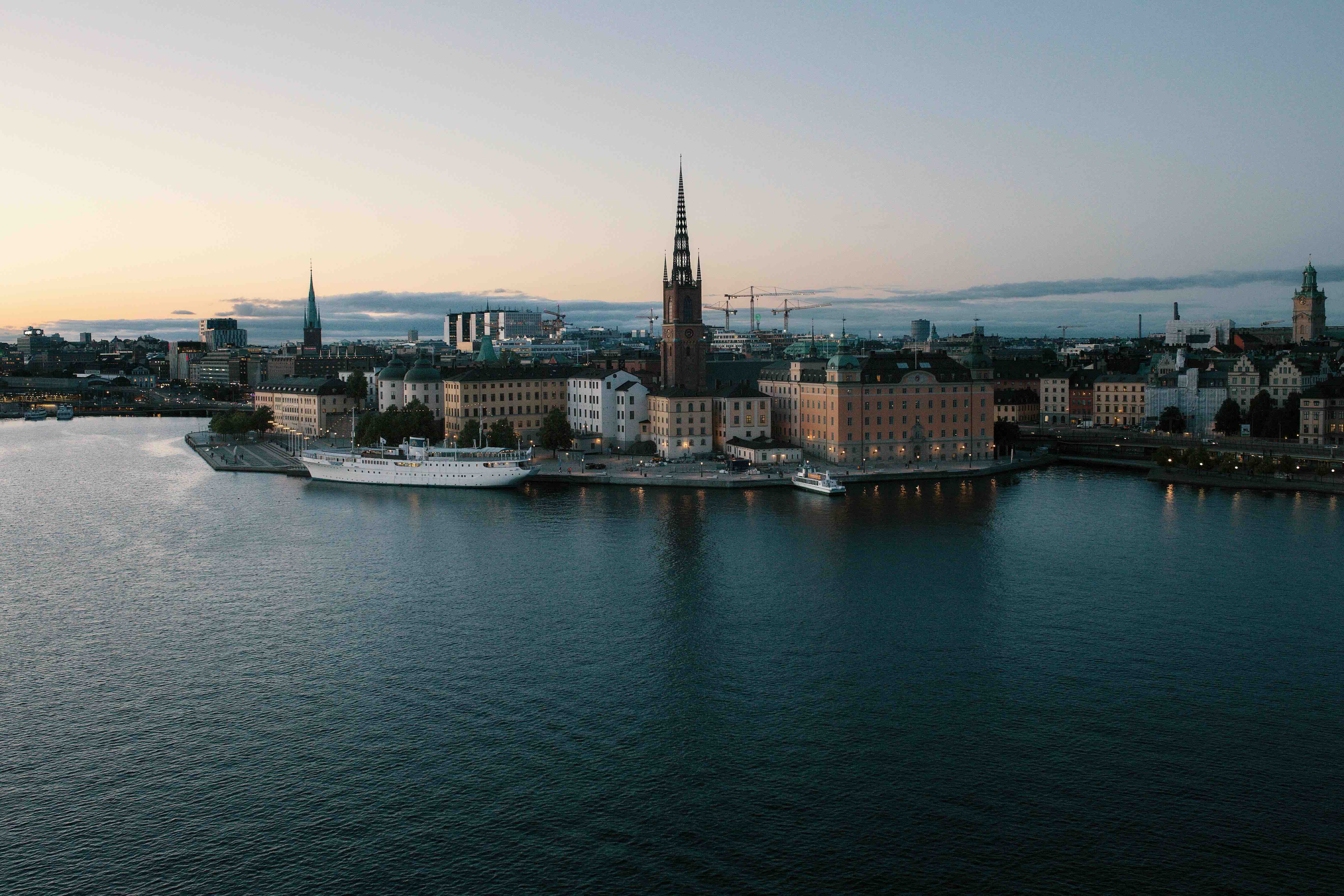 The Riddarholmen skyline of Stockholm at dusk, with the openwork iron spire of Riddarholmen Church rising above the waterfront across the water