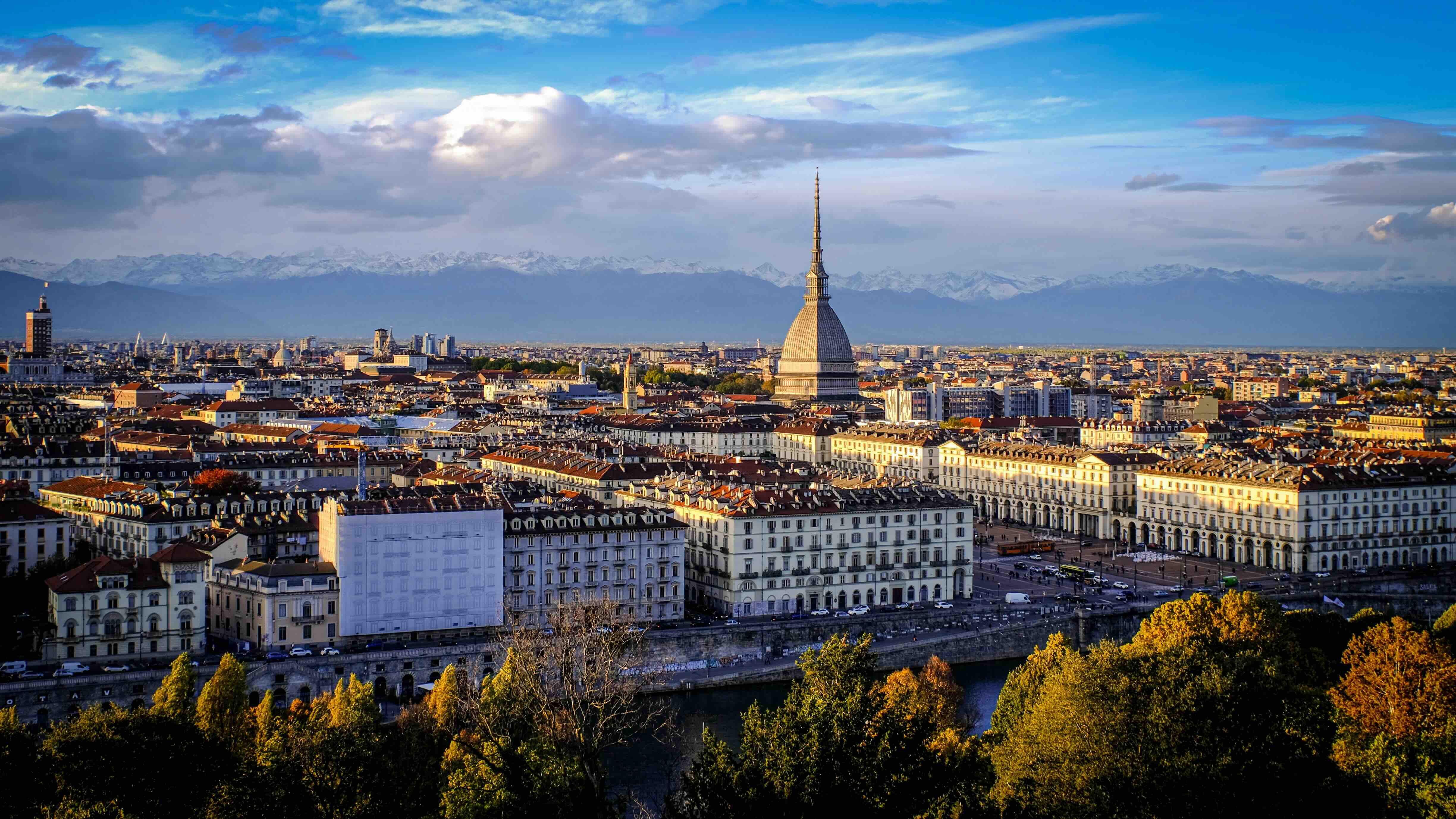 The rooftops of Turin from the hills across the Po, with the spire of the Mole Antonelliana rising above the city and the snow-capped Alps on the horizon